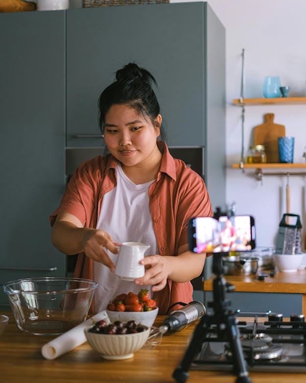 Een vrouw staat in de keuken en houdt een kannetje omhoog terwijl ze zichzelf filmt. Een vrouw staat in de keuken en houdt een kannetje omhoog terwijl ze zichzelf filmt.